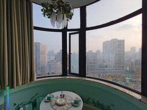 A room with a large window, a table with a tea set, and a view of a cityscape. - Meisuguan Apartment (Shanghai)
