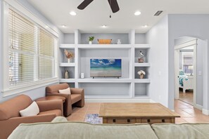 Ein Wohnzimmer mit Sofa, Fernseher, Regalen und Deckenventilator.