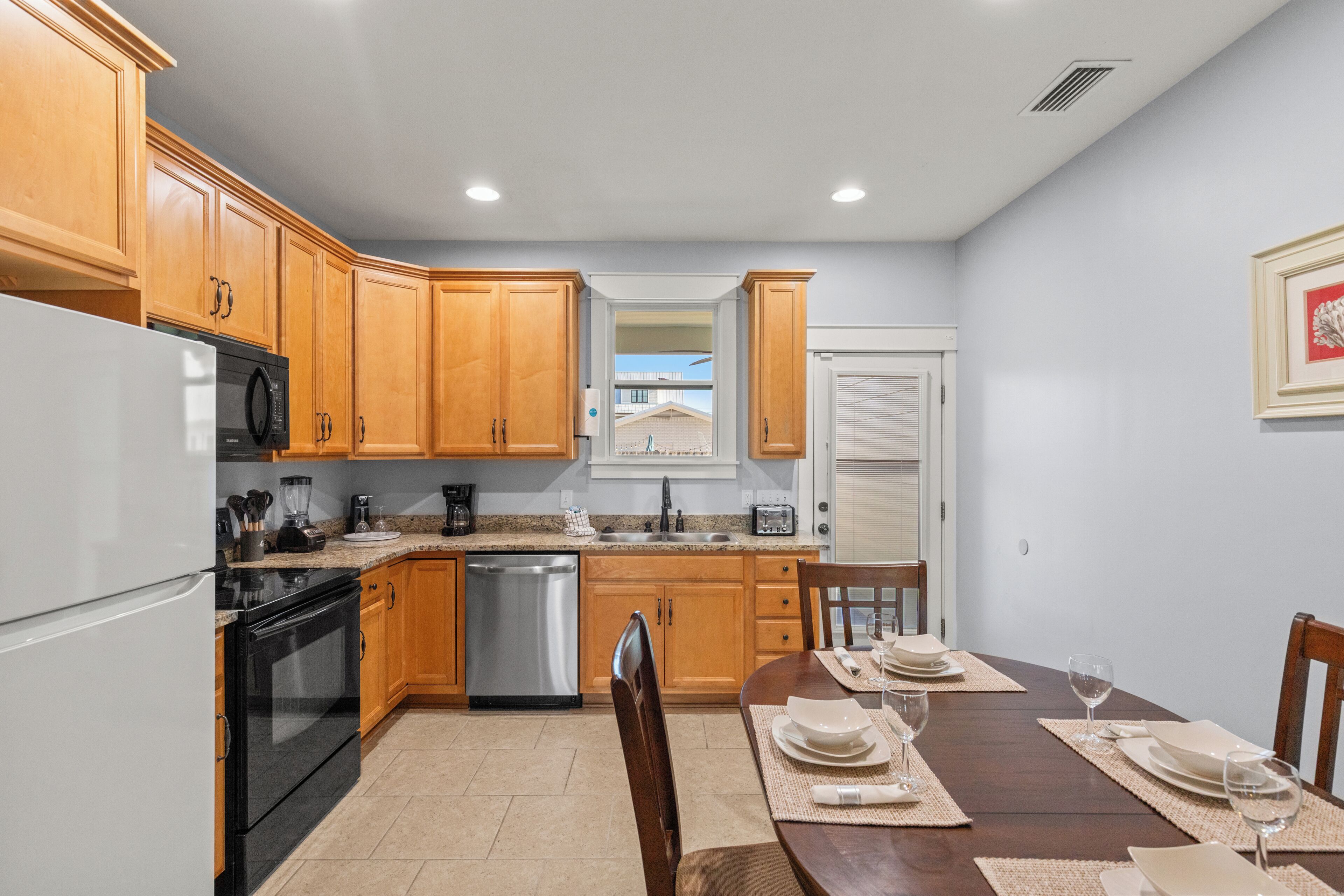A kitchen with wooden cabinets, a refrigerator, stove, dishwasher, and a dining area with a table set for two.