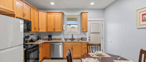 A kitchen with wooden cabinets, a refrigerator, stove, dishwasher, and a dining area with a table set for two.