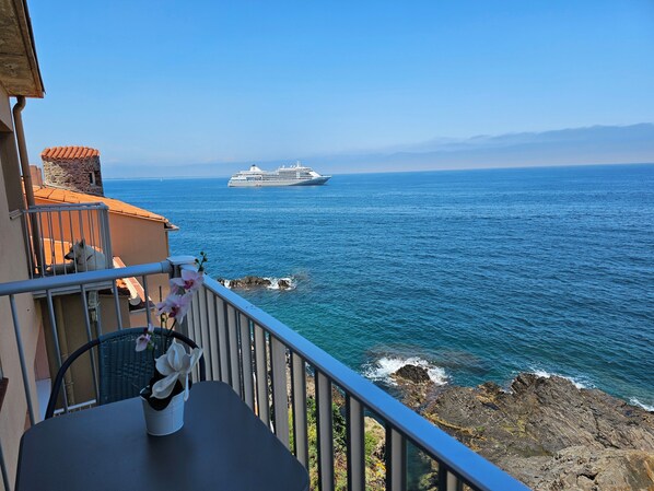Ein Balkon mit Meerblick, ein Kreuzfahrtschiff in der Ferne und ein Topf mit einer Orchidee.