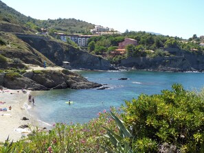 Eine Küstenlandschaft mit Strand, Felsen und Gebäuden im Hintergrund.