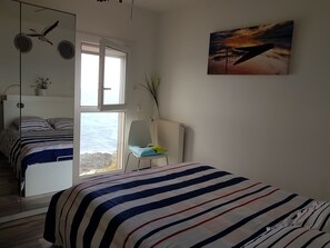 Ein Schlafzimmer mit Bett, Sessel, Fenster mit Meerblick und einem Bild an der Wand.