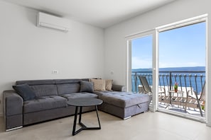 A modern living room with a grey sectional sofa, a small round table, and a balcony with a view of the sea. - Seaview Villa Diamond, 7-bedroom villa Just 500 Meters from the Beach (Dugi Rat)