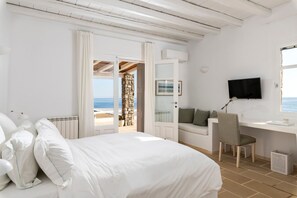 Ein Schlafzimmer mit Bett, Schreibtisch, Sessel und Fernseher, mit Blick aufs Meer.