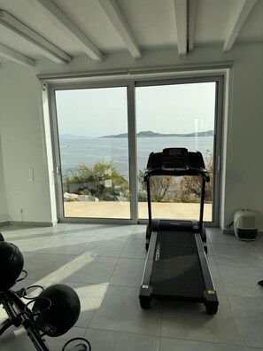 Ein Zimmer mit Laufband, Fitnessgeräten und einem großen Schiebeglastür, die Meerblick bietet.