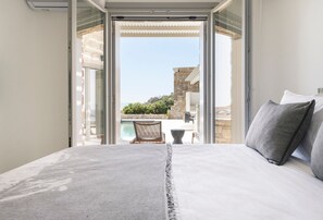 Ein Schlafzimmer mit einem großen Bett, Blick auf einen Pool und ein Steinhaus im Hintergrund.