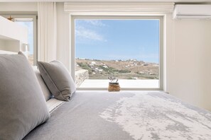Ein Schlafzimmer mit großem Fenster, einem Bett und Blick auf eine hügelige Landschaft.
