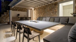 A modern outdoor dining area with a stone wall, a long table, and chairs. - Villa Poeme Kalo Livadi Mykonos (Mykonos)