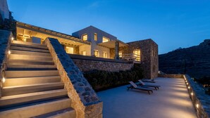 A modern building with a stone staircase leading to a rooftop area with lounge chairs. - Villa Poeme Kalo Livadi Mykonos (Mykonos)