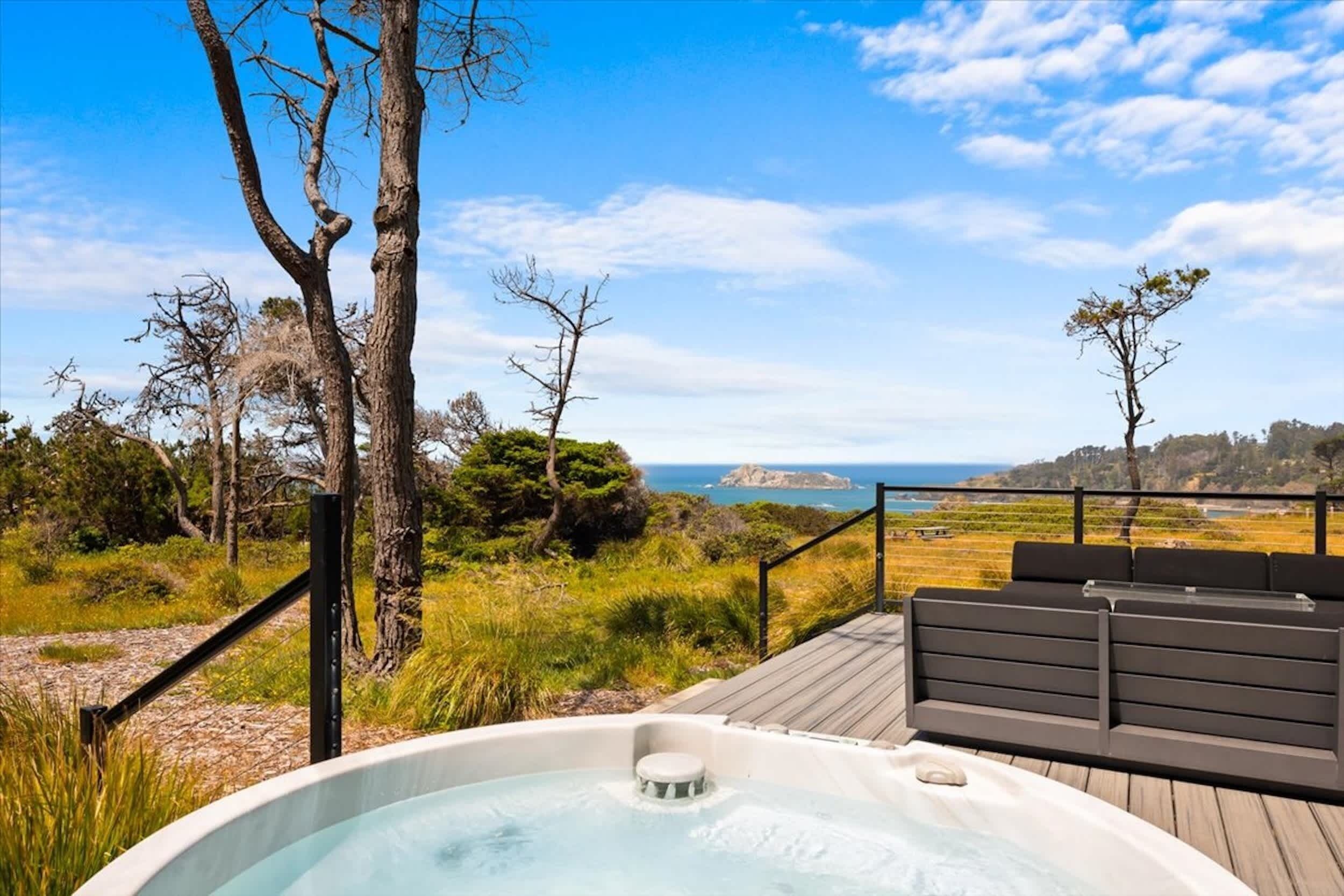 A hot tub on a deck with a view of the ocean and hills.