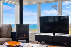 Ein Wohnzimmer mit Kamin, Fernseher und Meerblick.