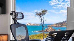 Ein Zimmer mit Blick auf das Meer, ein Sessel und ein Schreibtisch mit einem Computer.