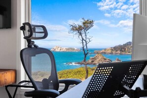 Ein Zimmer mit Blick auf das Meer, ein Sessel und ein Schreibtisch mit einem Computer.