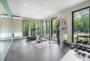 Ein modernes Fitnessstudio mit Trainingsgeräten, großen Fenstern und Blick auf Grünflächen.
