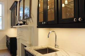 A kitchen with dark cabinets, a marble countertop, and a sink. - Grand Brownstone with Private Rooftop & Chef's Kitchen (Pittsburgh)