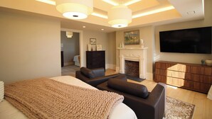 Un dormitorio moderno con una cama grande, chimenea, televisor y una zona de estar.