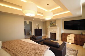 A modern bedroom with a large bed, a fireplace, a TV, and a seating area. - Grand Brownstone with Private Rooftop & Chef's Kitchen (Pittsburgh)