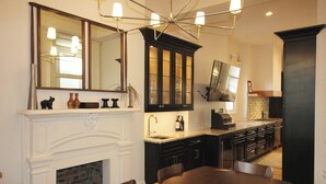 Una cocina con chimenea blanca, armarios oscuros, una mesa de comedor y un espejo grande sobre la encimera.
