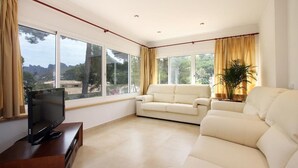 Un ampio soggiorno con una grande finestra, un televisore a schermo piatto su un mobile in legno e un divano color beige.