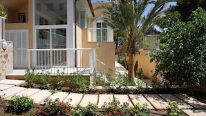 Un edificio a due piani con un balcone, una palma e un giardino con pietre e fiori.