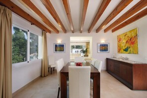 A dining area with a wooden ceiling, a dining table, chairs, a cabinet, and artwork on the walls. - Country Home "Can Medina" close to the Beach with Pool, Terrace & Garden (Cala Sant Vicenç)