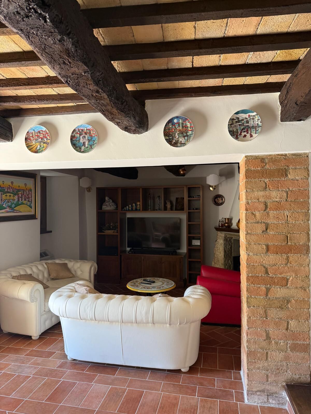 Una sala de estar con un sofá blanco, un sillón rojo, televisor y platos decorativos en la pared.
