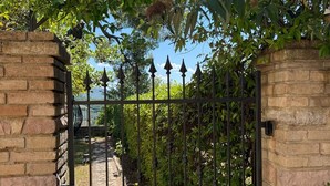 A gated entrance with a brick wall, a metal gate, and a pathway leading through a garden. - Terrace of Collepino | Panoramic Holiday Home in Umbria (Collepino)