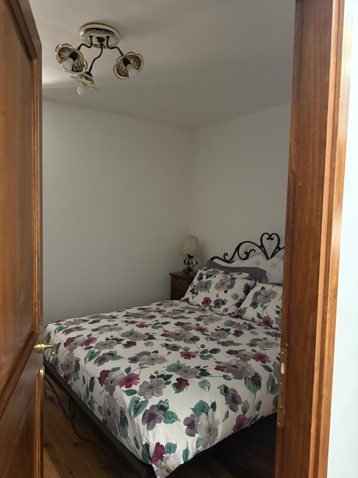 A bedroom with a floral bedspread, a nightstand with a lamp, and a ceiling light fixture.