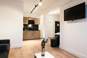 Ein modernes Wohnzimmer mit Flachbildfernseher, Essbereich und einer Küche im Hintergrund sowie ein kleiner Tisch mit einer Vase.