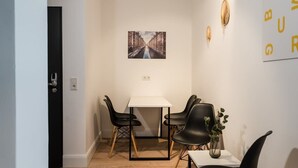 A small dining area with a white table and black chairs, a framed picture on the wall, and a vase with a plant on the table.
