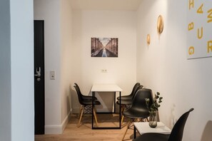 Ein kleiner Essbereich mit einem weißen Tisch und schwarzen Stühlen, einem gerahmten Bild an der Wand und einer Pflanze in einer Vase auf dem Tisch.