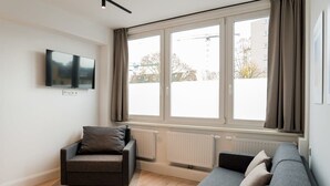 A modern living room with a sofa, a chair, a flat-screen TV, and large windows.