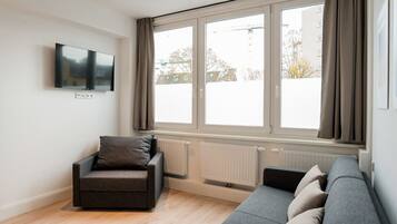 Ein modernes Wohnzimmer mit einer Couch, einem Sessel, einem Flachbildfernseher und großen Fenstern.