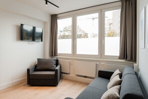 Ein modernes Wohnzimmer mit einer Couch, einem Sessel, einem Flachbildfernseher und großen Fenstern.