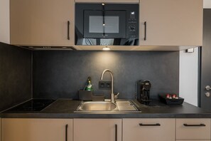 Eine moderne Küche mit integriertem Mikrowellenherd, einer Spüle aus Edelstahl, einer Kaffeemaschine und einem Wasserkocher.