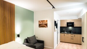 A compact room with a bed, a sofa, a kitchenette, and a wall-mounted artwork. - Standard Apartment - Homaris Apartments Hamburg Altona (Hamburg)
