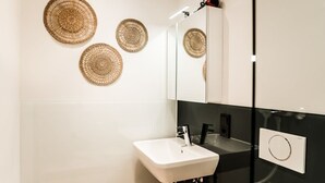 A modern bathroom with a white sink, black countertop, and three woven wall decorations. - Standard Apartment - Homaris Apartments Hamburg Altona (Hamburg)