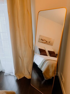 Ein Schlafzimmer mit Bett, Spiegel und einem Fenster mit Vorhang.