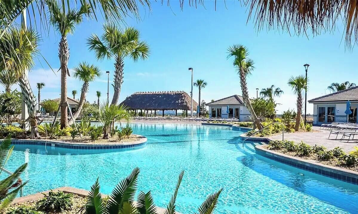 A pool surrounded by palm trees and a building with a thatched roof.