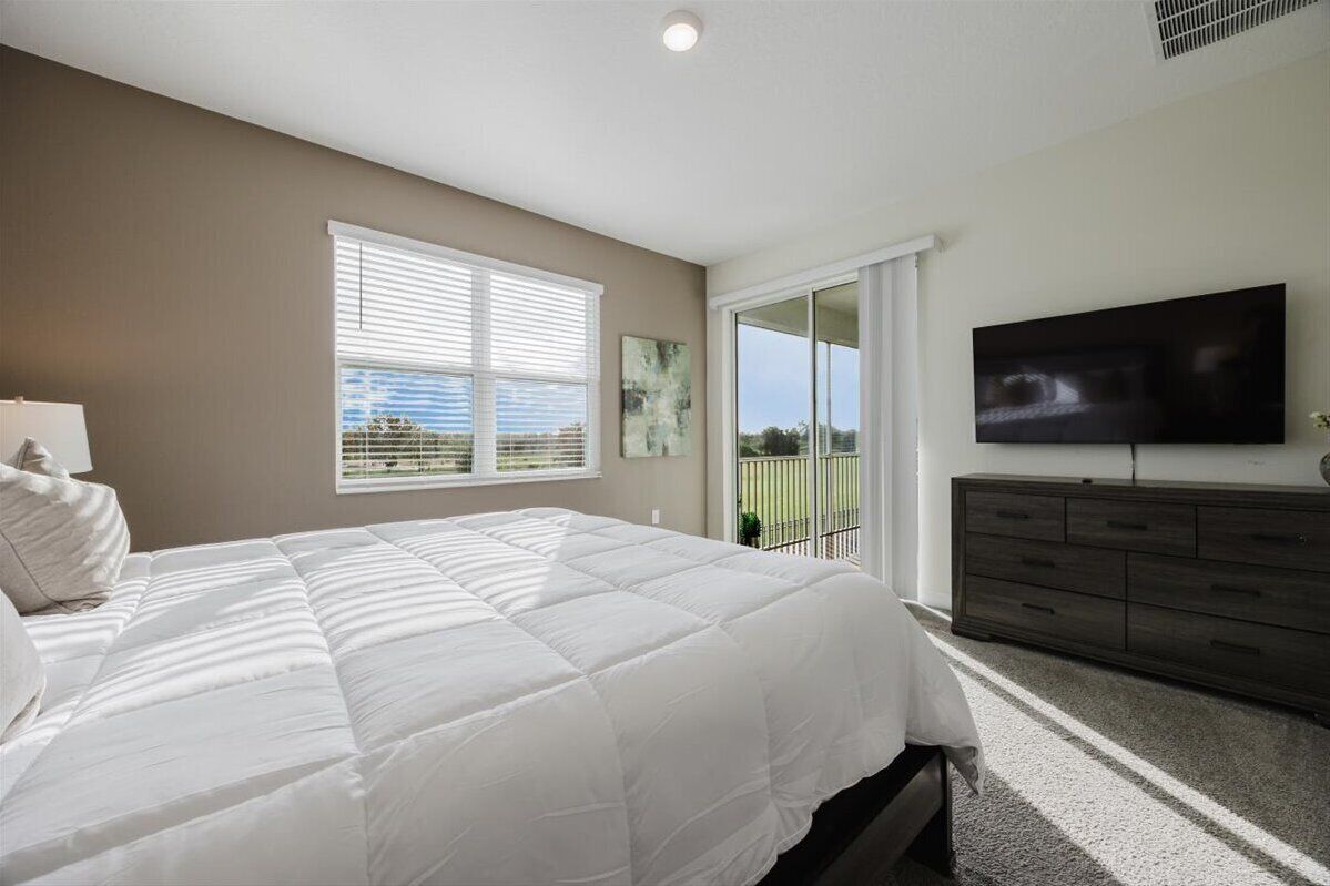 A bedroom with a bed, a dresser, a television, and a window with blinds.