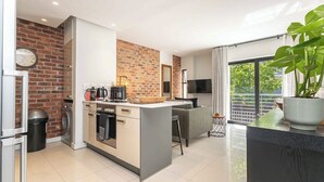A modern kitchen with a brick accent wall, a central island, and a large window overlooking a balcony. - One77 on Main (Green Point)