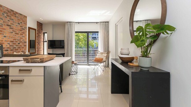 A modern kitchen with a brick wall, a large window, and a dining area with a chair and table. - One77 on Main (Green Point)