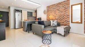 A modern living space with a kitchen, a grey sofa, a round coffee table, and a brick wall. - One77 on Main (Green Point)