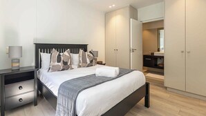 A modern bedroom with a bed, nightstands, a wardrobe, and a bathroom visible through an open door. - One77 on Main (Green Point)