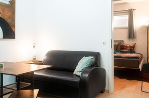 A compact living space with a black leather sofa, a small wooden table, and a bed with colorful bedding.