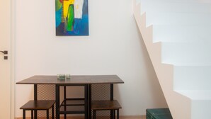 A room with a table and chairs, a staircase, and a painting on the wall.