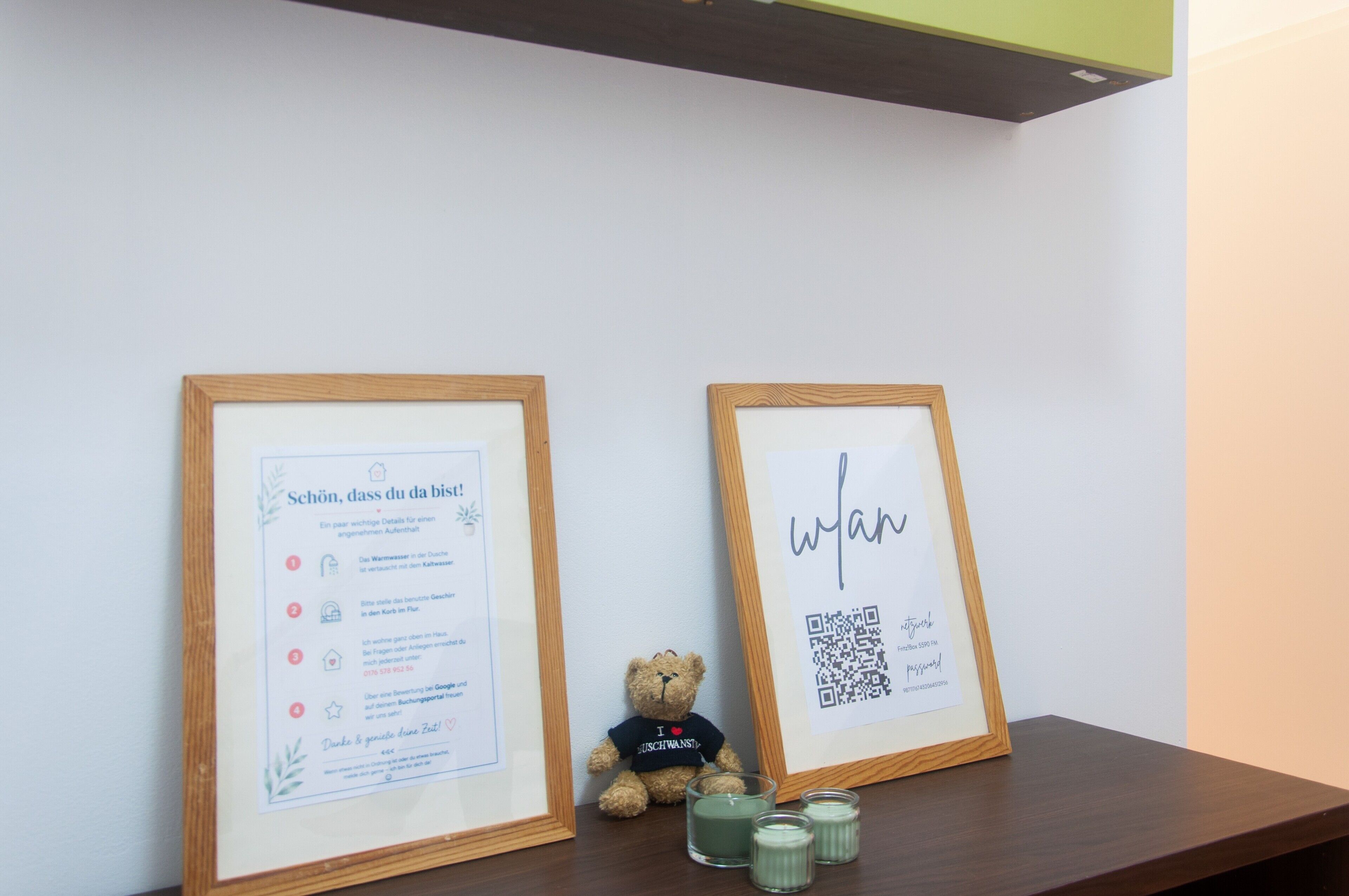Dos documentos enmarcados en un estante, uno con texto y otro con un código QR. También se ven un osito de peluche y velas.