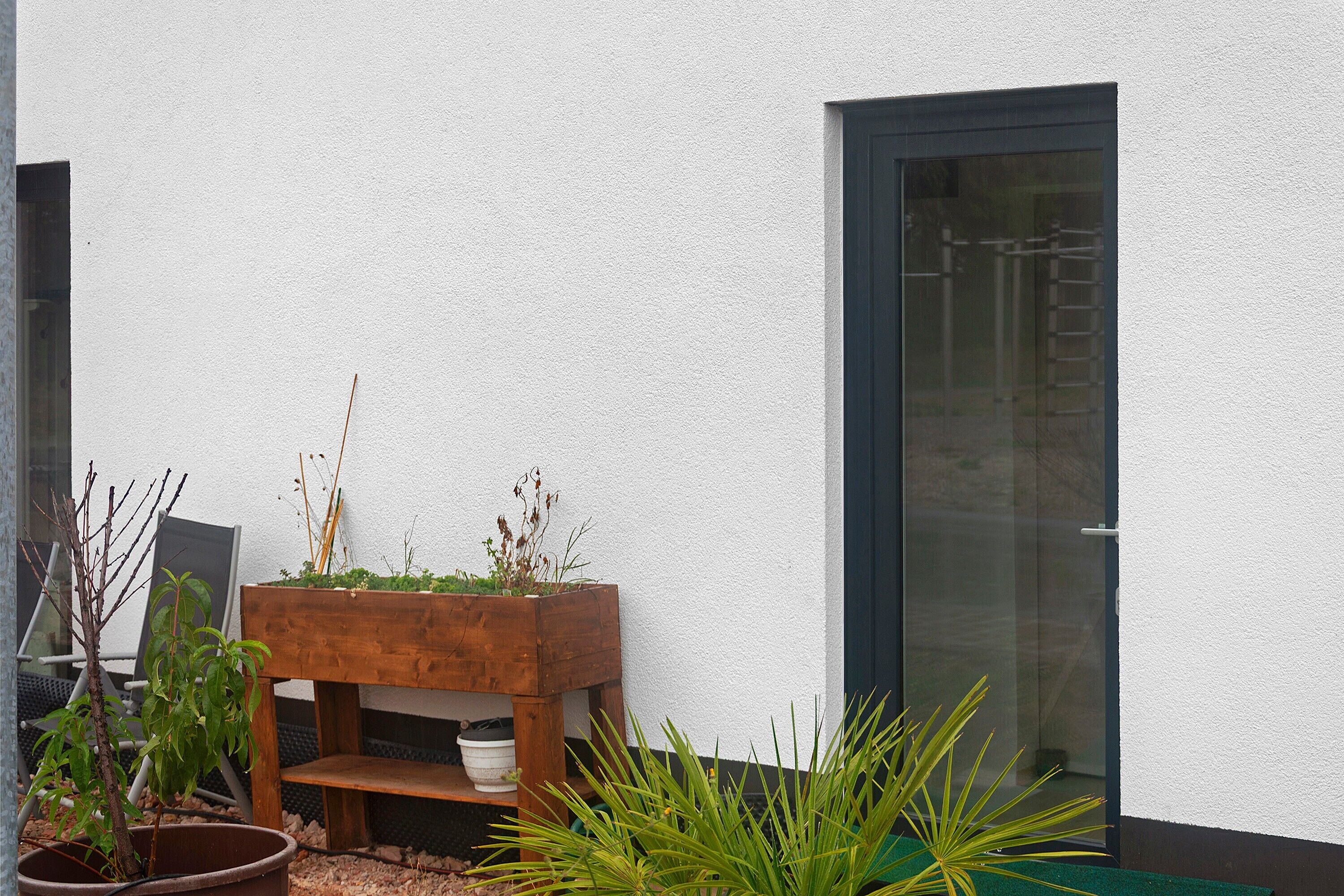A wooden planter box with plants against a white wall, next to a glass door.