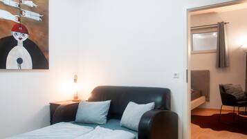 Ein Schlafzimmer mit einem Bett, einem Nachttisch, einer Lampe, einem Gemälde und Blick aus einem Fenster.